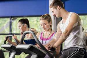 Trainer woman talking with a man doing exercise bike