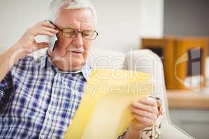 Senior man talking on mobile phone while looking at document
