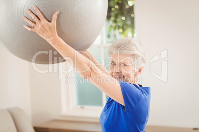 Senior woman lifting exercise ball while exercising