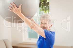 Senior woman lifting exercise ball while exercising