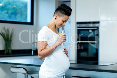 Pregnant woman drinking juice in kitchen