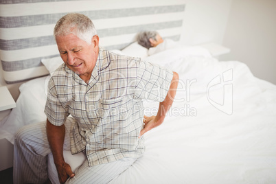 Senior man suffering from backache sitting on bed