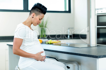 Pregnant woman sitting near kitchen worktop