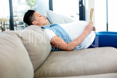 Pregnant woman reading a book while lying on sofa
