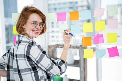 smiling hipster woman sticking notes on a notice board