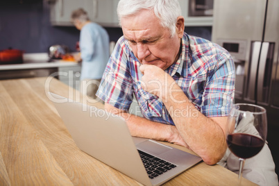 Senior man using laptop and woman working in kitchen