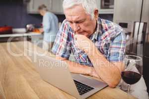 Senior man using laptop and woman working in kitchen