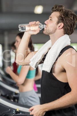 Athletic man drinking water while running on treadmill