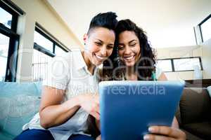 Lesbian couple sitting on sofa and using digital tablet