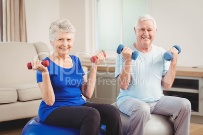 Portrait of senior couple sitting on fitness balls with dumbbell