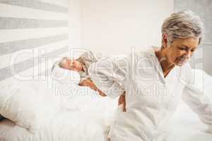 Senior woman suffering from backache sitting on bed