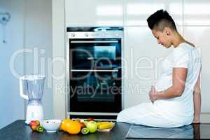 Pregnant woman sitting on kitchen worktop