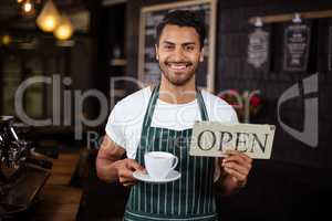 Smiling barista holding coffee and open sign