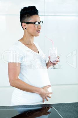 Pregnant woman drinking smoothie in kitchen