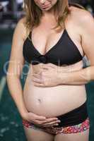 Smiling pregnant woman standing next to the pool