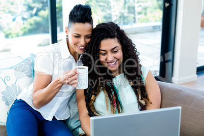 Happy lesbian couple having coffee and using laptop
