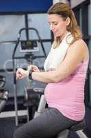 Pregnant woman on exercise bike using smartwatch