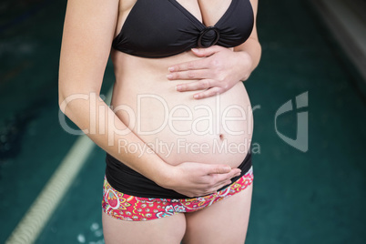Mid section of pregnant woman standing next to the pool