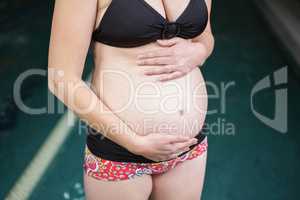 Mid section of pregnant woman standing next to the pool