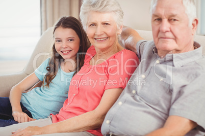 Grandparents and granddaughter sitting together on sofa