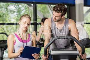 Trainer woman talking with a man doing exercise bike