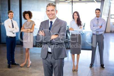 Businessman smiling at camera while his colleagues standing in b