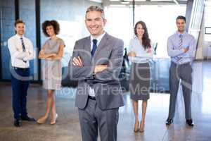 Businessman smiling at camera while his colleagues standing in b