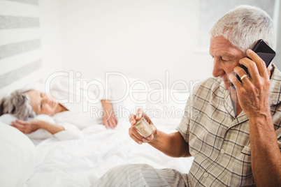 Senior man looking at pill bottle and talking on phone