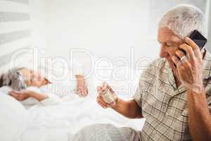 Senior man looking at pill bottle and talking on phone