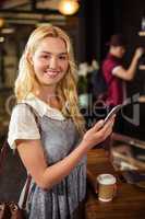 Smiling blonde drinking coffee and using smartphone