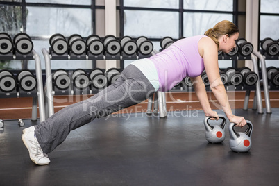 Determined woman planking with kettlebells