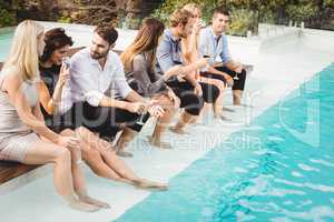Young people sitting by swimming pool