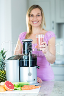 Blonde woman holding a smoothie glass in the kitchen