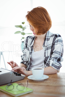smiling hipster woman drinking coffee and typing on her typewrit