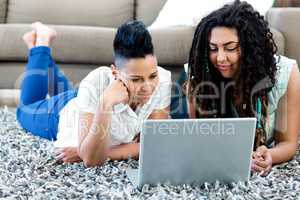 Smiling lesbian couple lying on rug and using laptop