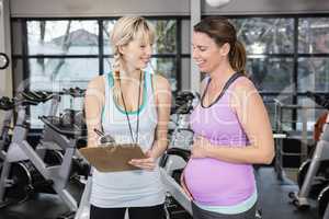 Smiling trainer showing clipboard to pregnant woman