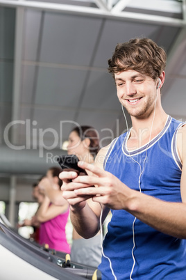 Smiling muscular man on treadmill listening to music