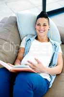 Portrait of pregnant woman reading a book while lying on sofa