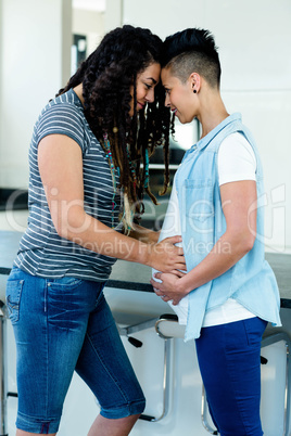 Pregnant lesbian couple embracing in kitchen