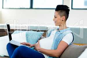 Pregnant woman relaxing on sofa with her laptop