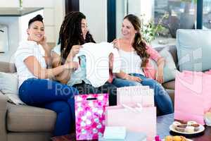 Three women sitting on sofa and looking at babys clothes