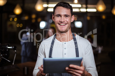 Smiling barista holding tablet and looking at the camera