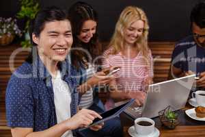 Smiling friends enjoying coffee together and using technologies