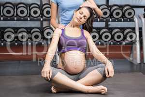 Trainer helping pregnant woman stretching her neck