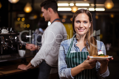 Pretty barista holding dessert and smiling at the camera