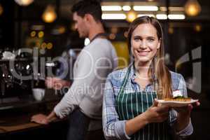 Pretty barista holding dessert and smiling at the camera