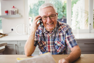 Senior man looking at a document while taking on phone