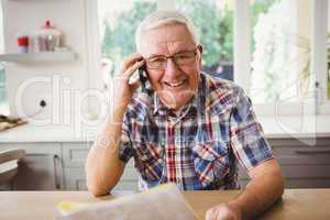 Senior man looking at a document while taking on phone