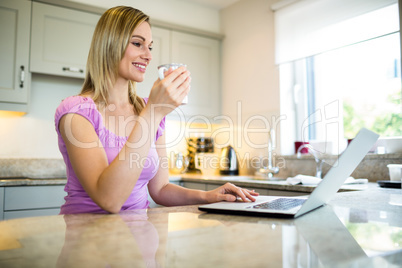 Pretty blonde woman having coffee and using laptop