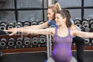 Trainer helping pregnant woman exercising on an exercise ball